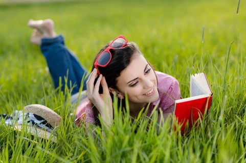 Young woman lying in meadow and reading a book,