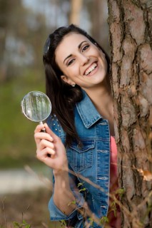 Woman looks at tree trunk under the magnifying glass,