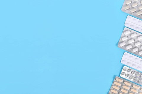 Different capsules and pills in blister packs on right side of blue background with copy space,