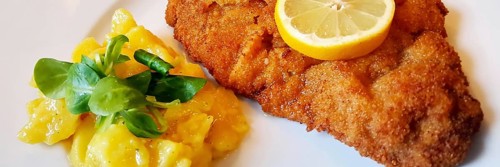 Delicious golden-brown fried Wiener Schnitzel with potato salad and a slice of lemon on a white plate,