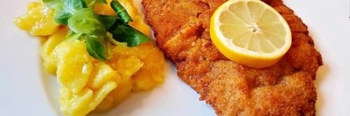 Delicious golden-brown fried Wiener Schnitzel with potato salad and a slice of lemon on a white plate,