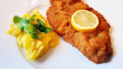 Delicious golden-brown fried Wiener Schnitzel with potato salad and a slice of lemon on a white plate,