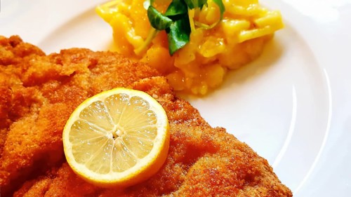 Delicious golden-brown fried Wiener Schnitzel with potato salad and a slice of lemon on a white plate,
