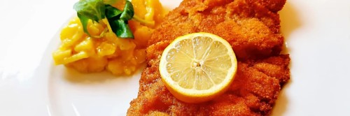 Delicious golden-brown fried Wiener Schnitzel with potato salad and a slice of lemon on a white plate,