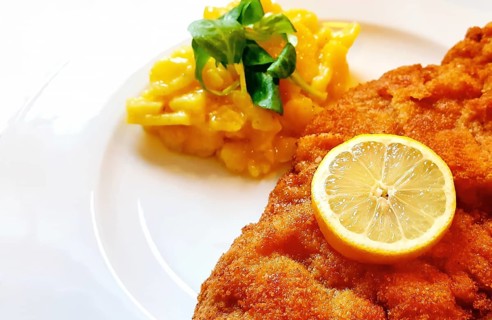Delicious golden-brown fried Wiener Schnitzel with potato salad and a slice of lemon on a white plate,