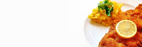 Delicious golden-brown fried Wiener Schnitzel with potato salad and a slice of lemon on a white plate,