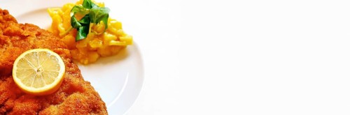 Delicious golden-brown fried Wiener Schnitzel with potato salad and a slice of lemon on a white plate,