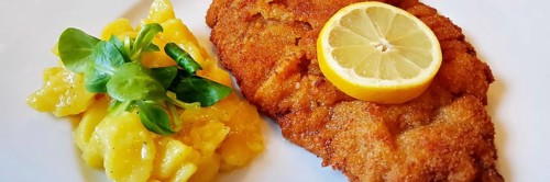 Delicious golden-brown fried Wiener Schnitzel with potato salad and a slice of lemon on a white plate,