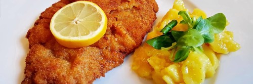 Delicious golden-brown fried Wiener Schnitzel with potato salad and a slice of lemon on a white plate,