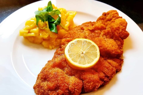 Delicious golden-brown fried Wiener Schnitzel with potato salad and a slice of lemon on a white plate,