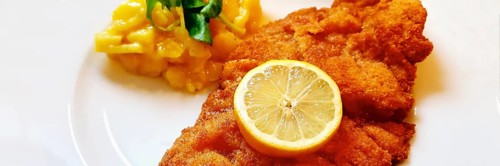 Delicious golden-brown fried Wiener Schnitzel with potato salad and a slice of lemon on a white plate,