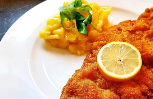 Delicious golden-brown fried Wiener Schnitzel with potato salad and a slice of lemon on a white plate,