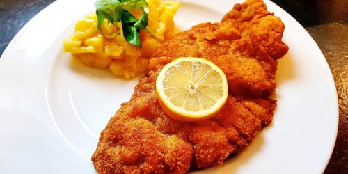 Delicious golden-brown fried Wiener Schnitzel with potato salad and a slice of lemon on a white plate,