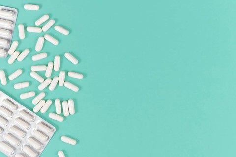 White capsule pills on left side of mint green background with blank copy space,