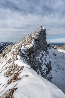 Mountaineer stretching his arms in the air, standing on a snow-covered rocky ridge