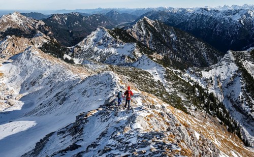 Two mountaineers on the narrow rocky snowy ridge of the Ammergauer Hochplatte, view towards Loesertaljoch