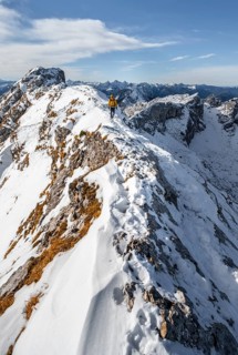 Climbers on a narrow rocky snowy ridge, behind peak crow