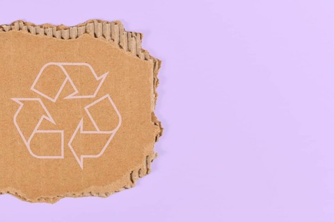 Piece of cardboard with recycling arrow sign on violet blue background with copy space,