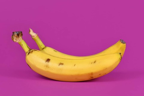 Ripe banana fruits with peel on purple background,