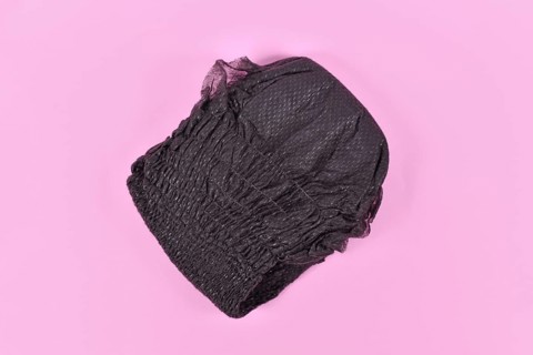 Black folded diaper for adult women on pink background,
