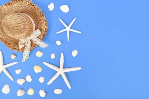 White starfish, seashells and summer straw hat on side of blue background with copy space