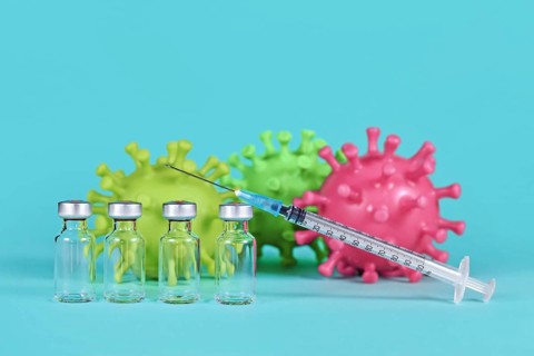 4 vaccine vials with syringes and corona virus models in background,