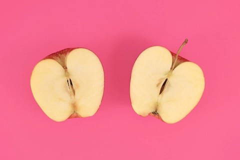 Apple cut into half on pink background,