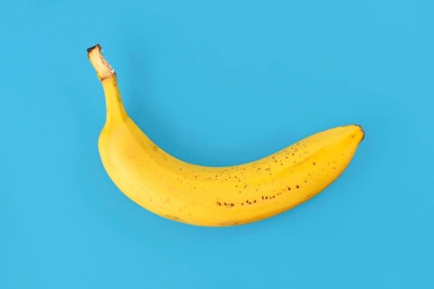 Single ripe banana with peel on blue background,