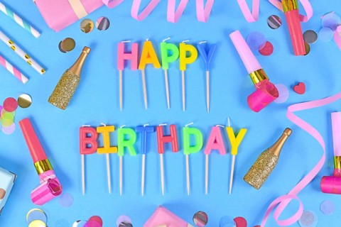Party flat lay with Happy Birthday candles, confetti and paper streamers on blue background