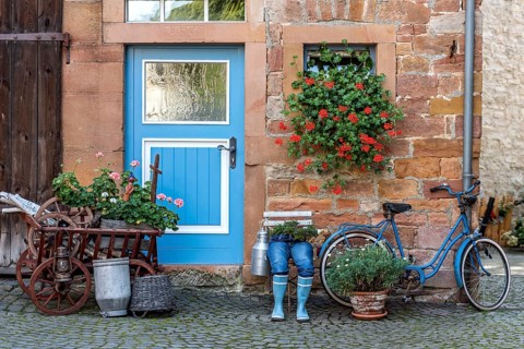 Curious decoration on a front door, blue jeans trousers in rubber boots with flower pot
