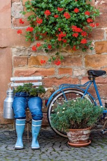 Curious decoration on a front door, blue jeans trousers in rubber boots with flower pot