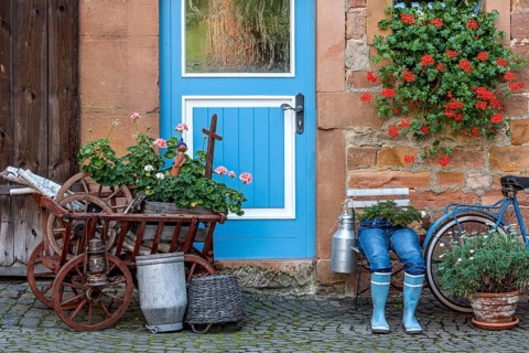 Curious decoration on a front door, blue jeans trousers in rubber boots with flower pot