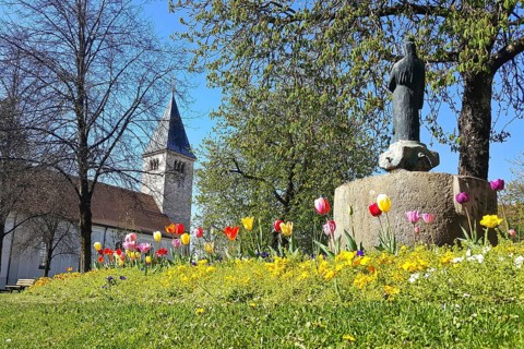 St. Michael's Church and the war memorial in the centre of Peiting. Tulips in the foreground. Bavaria, Germany
