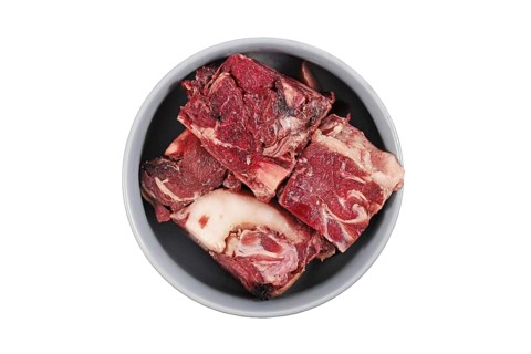 Dog bowl with big red chunks of meat with fat used for raw biologically appropriate feeding on white background,