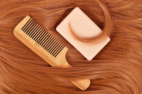 Solid shampoo bar and wooden comb on red hair. Concept for eco friendly healthy hair care routine,
