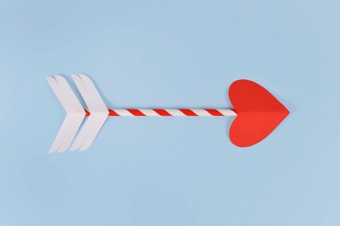 Simple paper cupid love arrow with heart shaped tip on blue background,