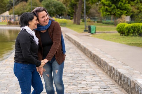 Lesbian couple in a park holding hands laughing. Copy space,