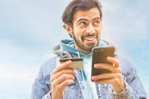 Latin man using credit card to make online payment on smartphone. mixed-race man using cellphone for shopping online. Guy using smart phone to check credit card transactions from app. Copy space,