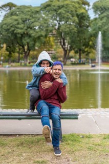 Gay Latino male couple sitting on a bench in a park laughing,