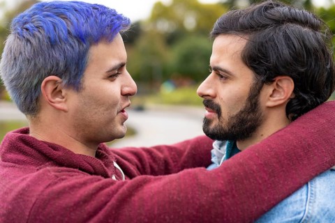 Latin gay couple hugging in a park looking at each other about to kiss,
