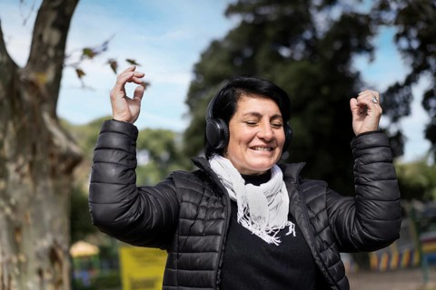 Latin woman listening to music outdoors with headphones. Expression of happiness, winning attitude. Copy space