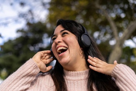Young latin woman listening to music outdoors with headphones. Expression of happiness, winning attitude. Copy space