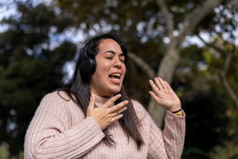 Young latin woman listening to music outdoors with headphones. Expression of happiness, winning attitude. Copy space