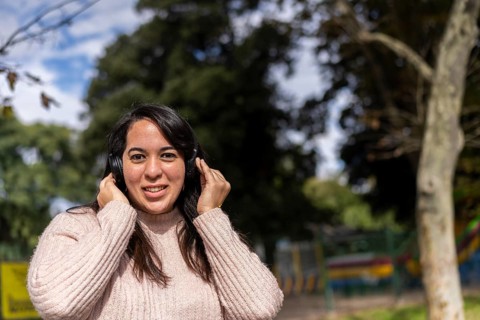 Young latin woman listening to music outdoors with headphones. Expression of happiness, winning attitude. Copy space