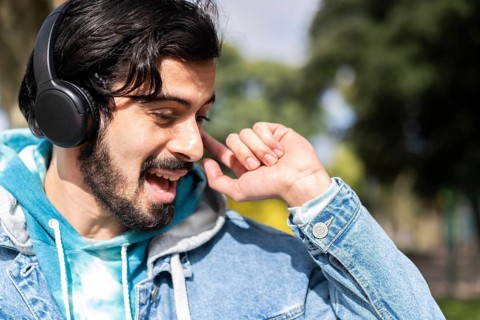 Young latin man listening to music outdoors with headphones. Expression of happiness, winning attitude