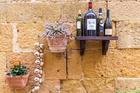 Wine bottles, flower box and garlic as decoration on a house wall in the centre of Pienza