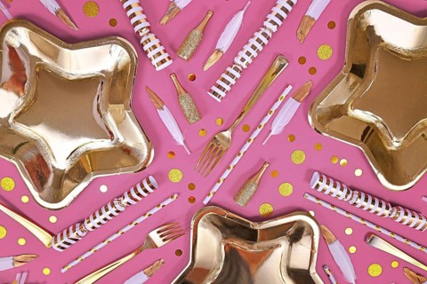 Party flat lay with golden and white decoration like plates, confetti and feathers on pink background