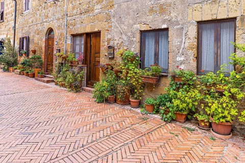 Old stone houses decorated with flower pots, diagonally laid brick pavement