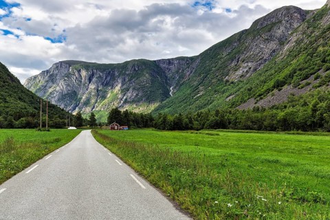 Single-lane country road through valley, typical landscape with high mountains