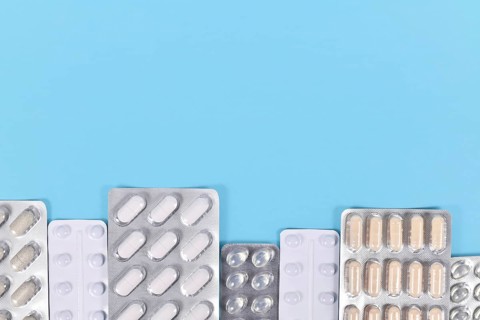 Blister packs with various pills and capsules at bottom of blue background with copy space,